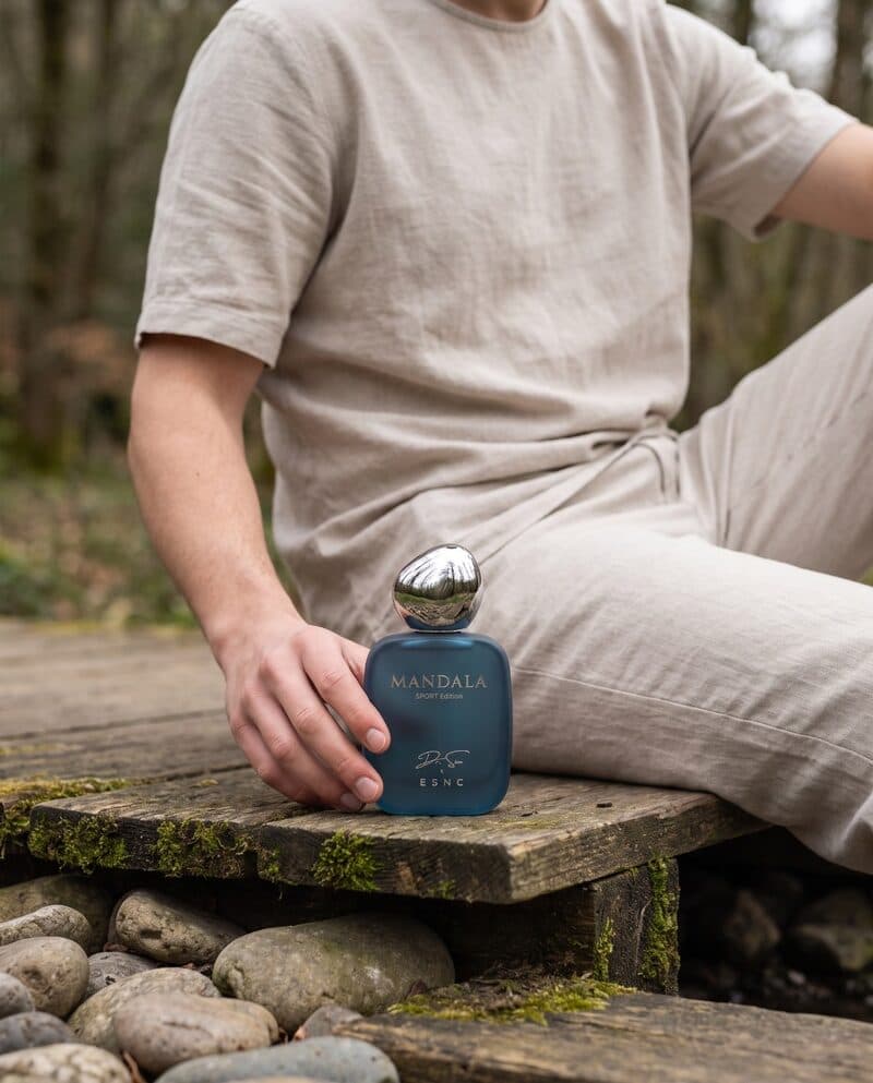 A person sitting outdoors on a stone ledge, holding an ESNC bottle